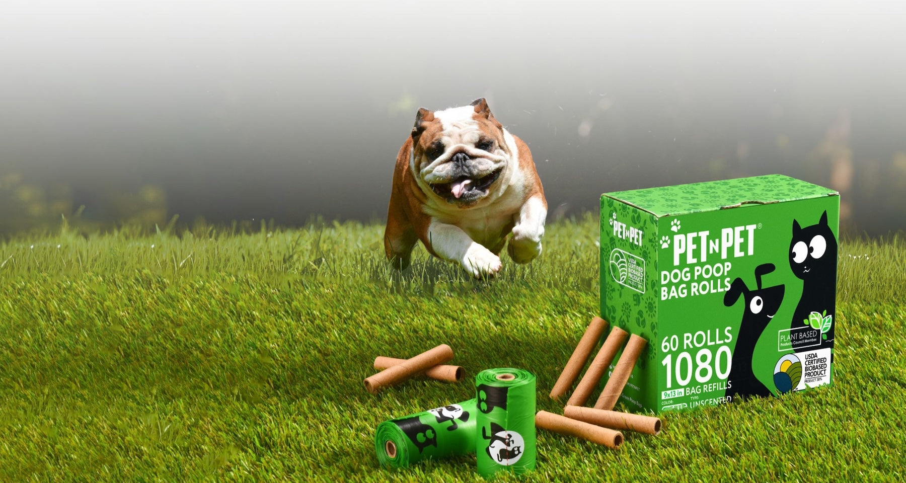 Dog playing with dog toys on grass next to a box of Pet-Pet dog poop bags.
