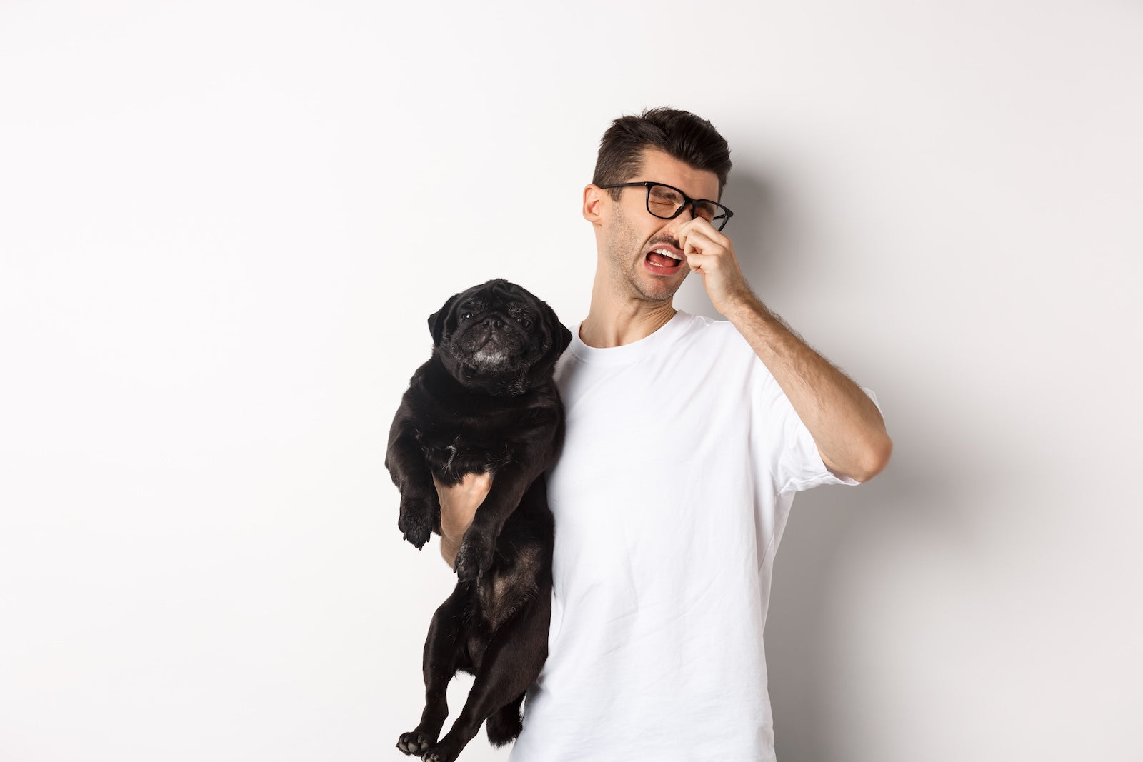 Man holding a black pug while pinching his nose from the dog’s bad breath, illustrating the problem of foul-smelling breath in dogs.