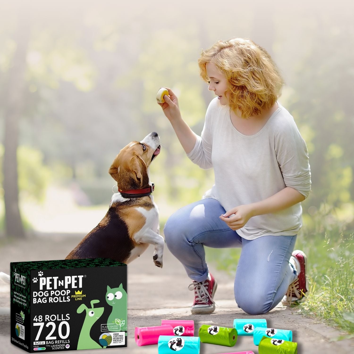Woman playing with a dog in a park, with a box of Pet 'N Pet dog waste bags in the foreground.