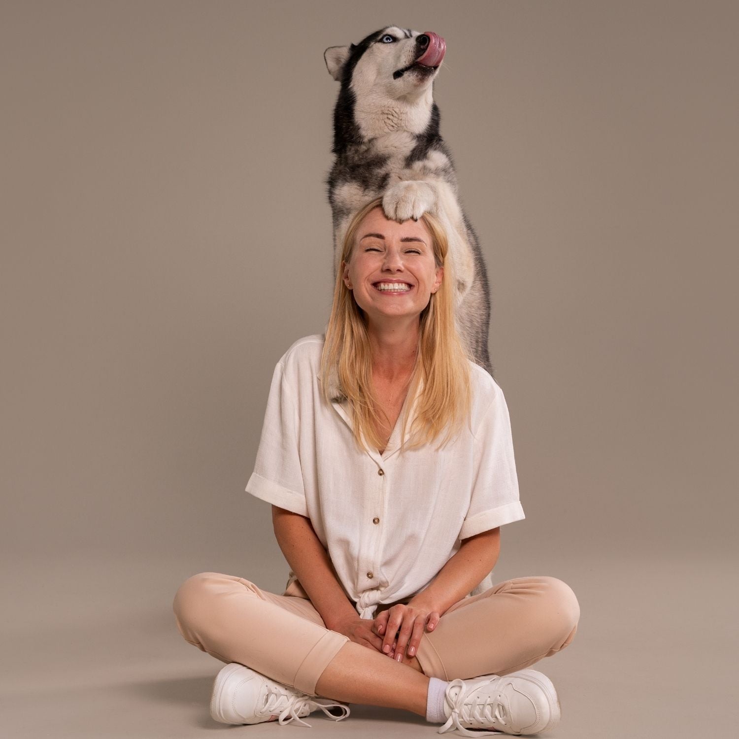 Woman sitting with a dog on her head against a beige background